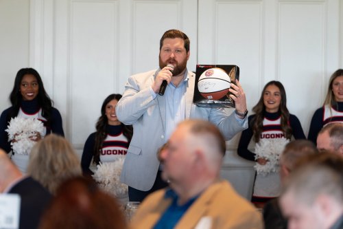 UConn Game Day Conor holding up a basketball for the auction, with UConn cheerleaders behind him.