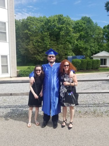 William Coons in a blue graduation gown and cap, hugging his sister, Kelly Coons, and his mother, Mary Coons, at his high school graduation at Franklin Academy.