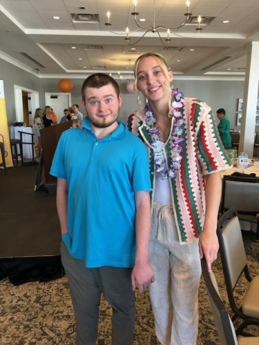 Kevin Coons, wearing a sky blue shirt, with Paige Bueckers, who is wearing a purple lei and a striped sweater.