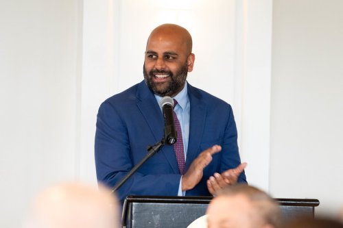 Hartford mayor Arunan Arulampalam at the podium in a dark blue suit, clapping.