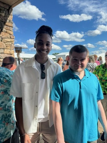 Kevin Coons, wearing a sky blue shirt, standing with a UConn women's basketball player wearing a plain white button-down shirt.